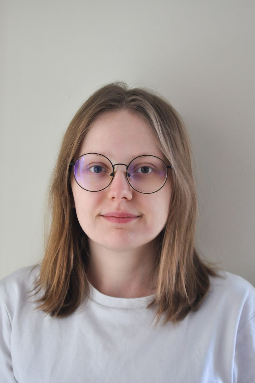 A portrait of Agata Lech against a light, uniform background. She has fair skin and straight, shoulder-length dark blonde hair. She wears large glasses with thin, black, round frames. She is dressed in a plain white T-shirt. She looks directly into the camera with a gentle, calm smile.